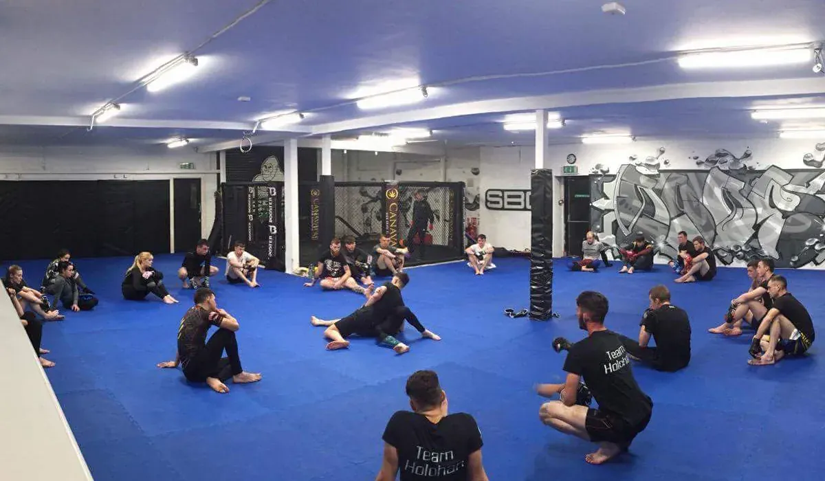 An MMA class on the blue mats, with the cage and striking area behind